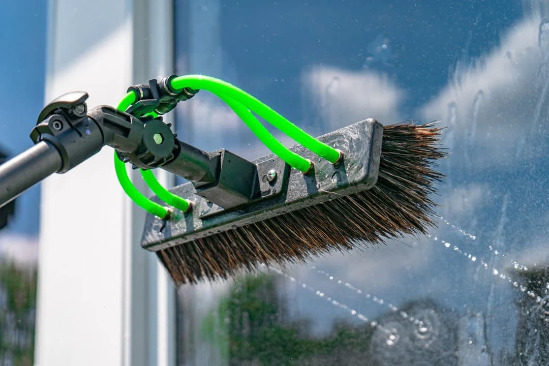 Window cleaning tool with a brush head and green handle, capturing streak-free shine.