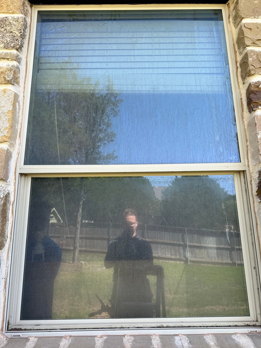 Window reflection showing trees and a person standing outside in natural light.