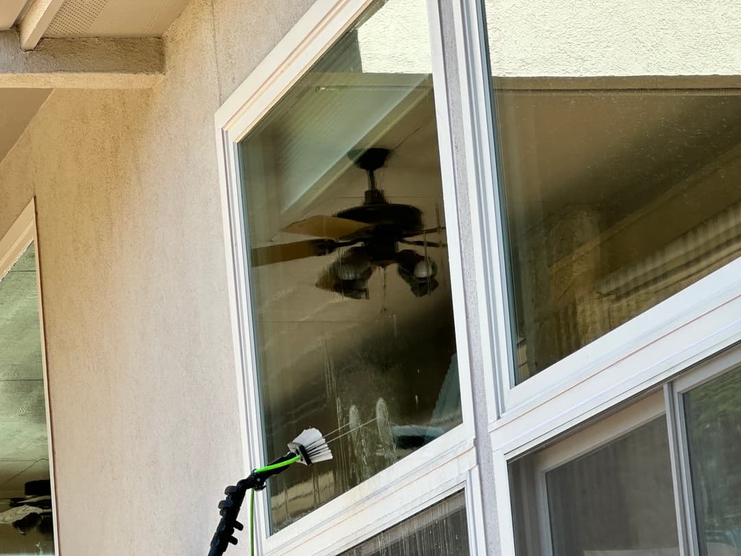 Window cleaning with a pressure washer reflecting a ceiling fan in a sunny environment.