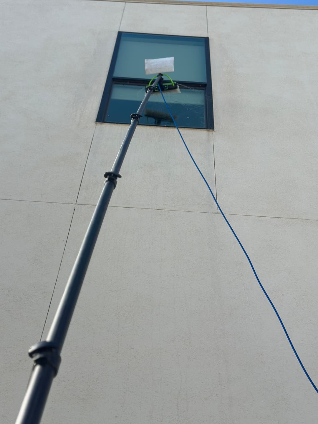 Window cleaner using a long pole to wash a high-rise window on a sunny day.