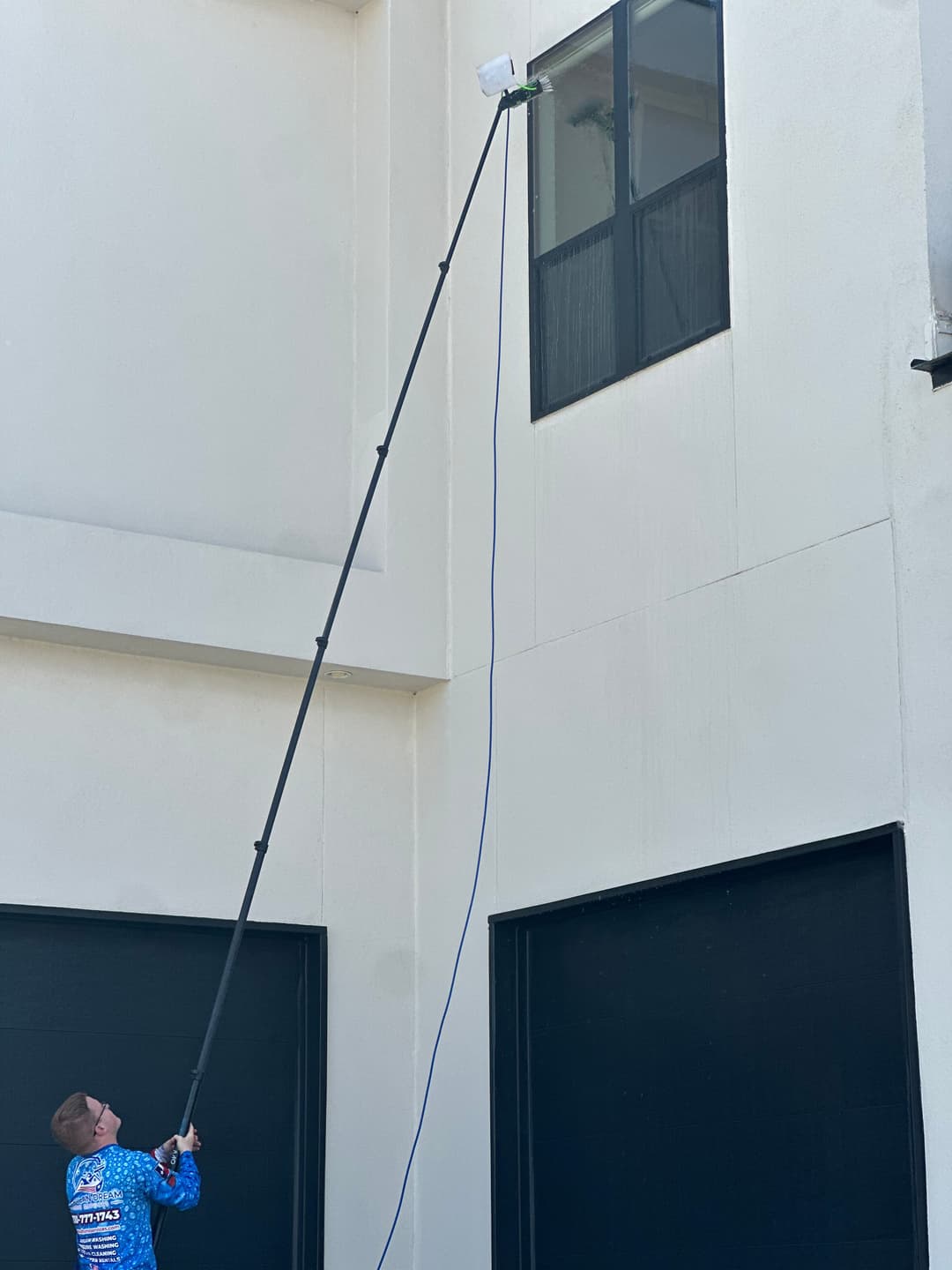 Person using a pole to clean a high window on a building's exterior.