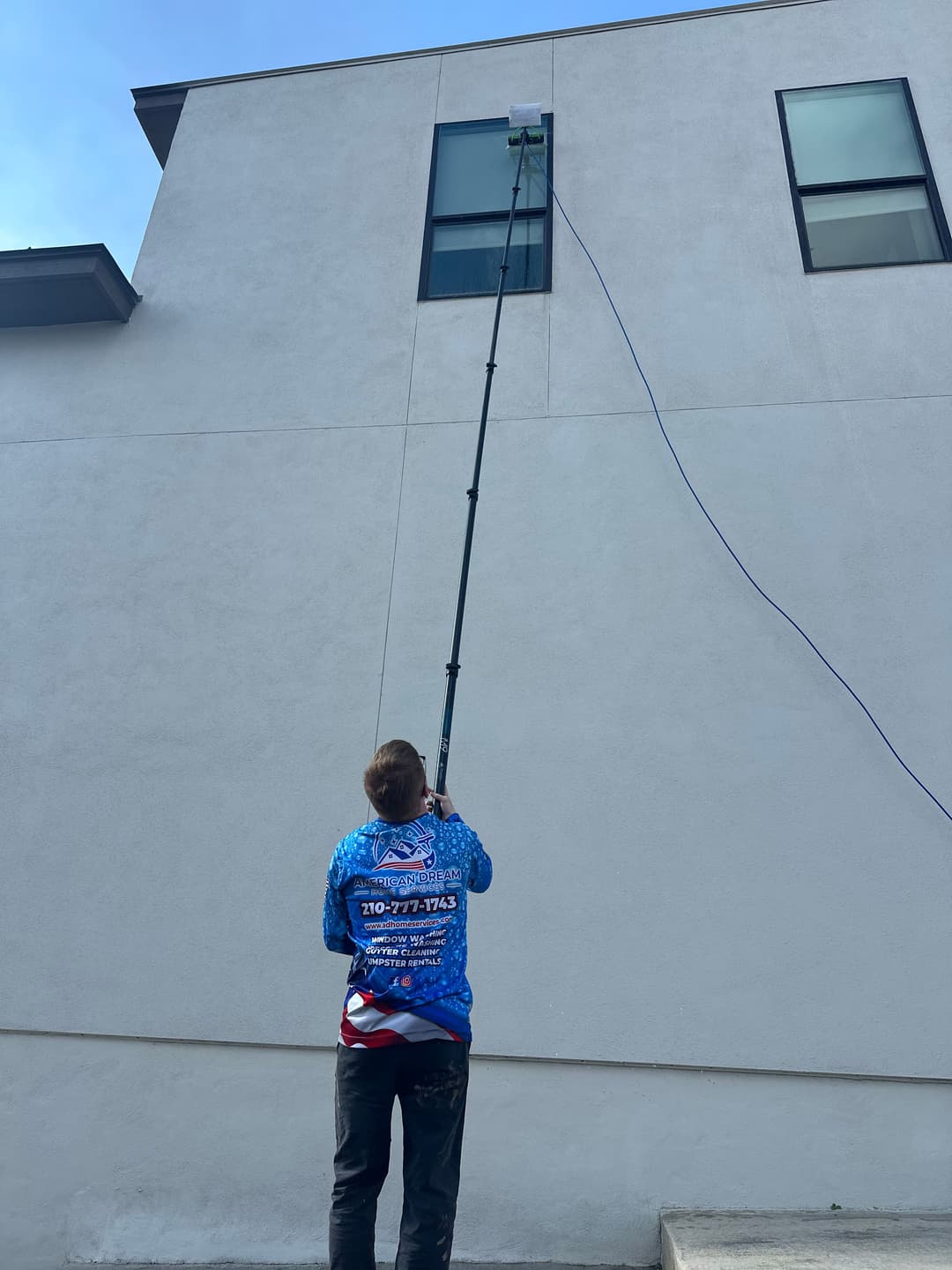 Person using a pole to clean windows on a building exterior under a blue sky.