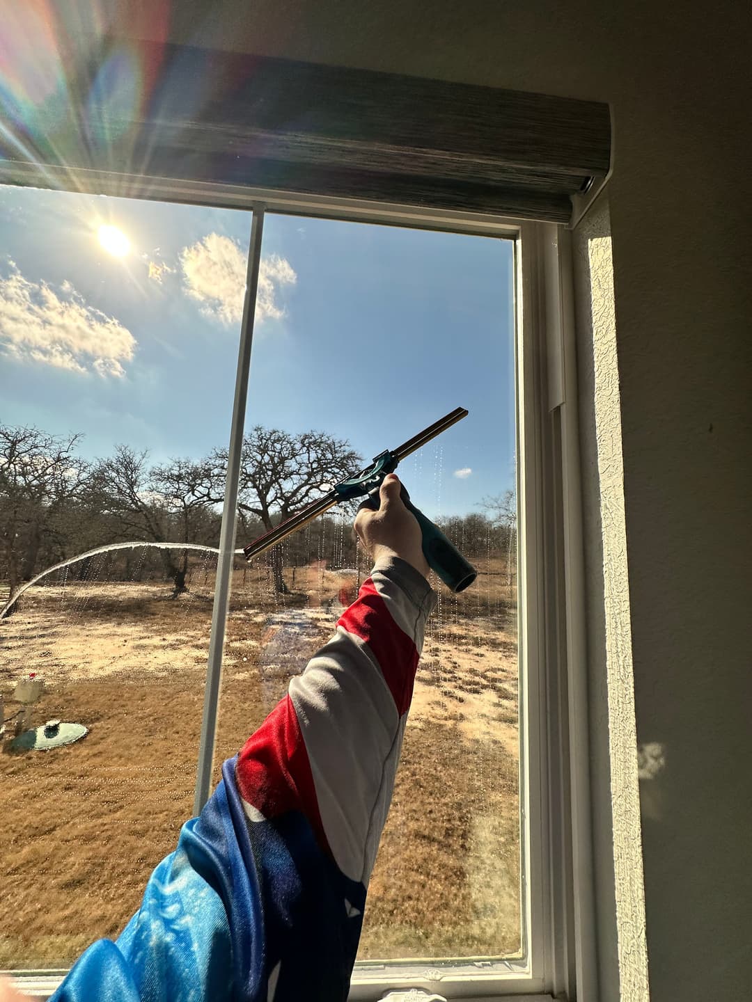 Person cleaning a window with a spray gun, sunlight shining through the glass.
