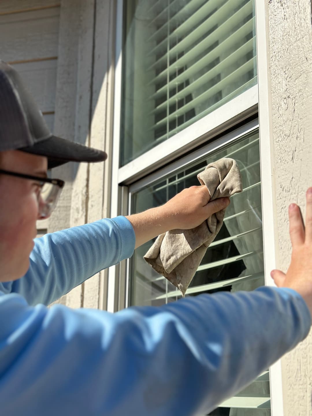 Person cleaning a window with a cloth, sunlight shining on the scene, showcasing home maintenance.