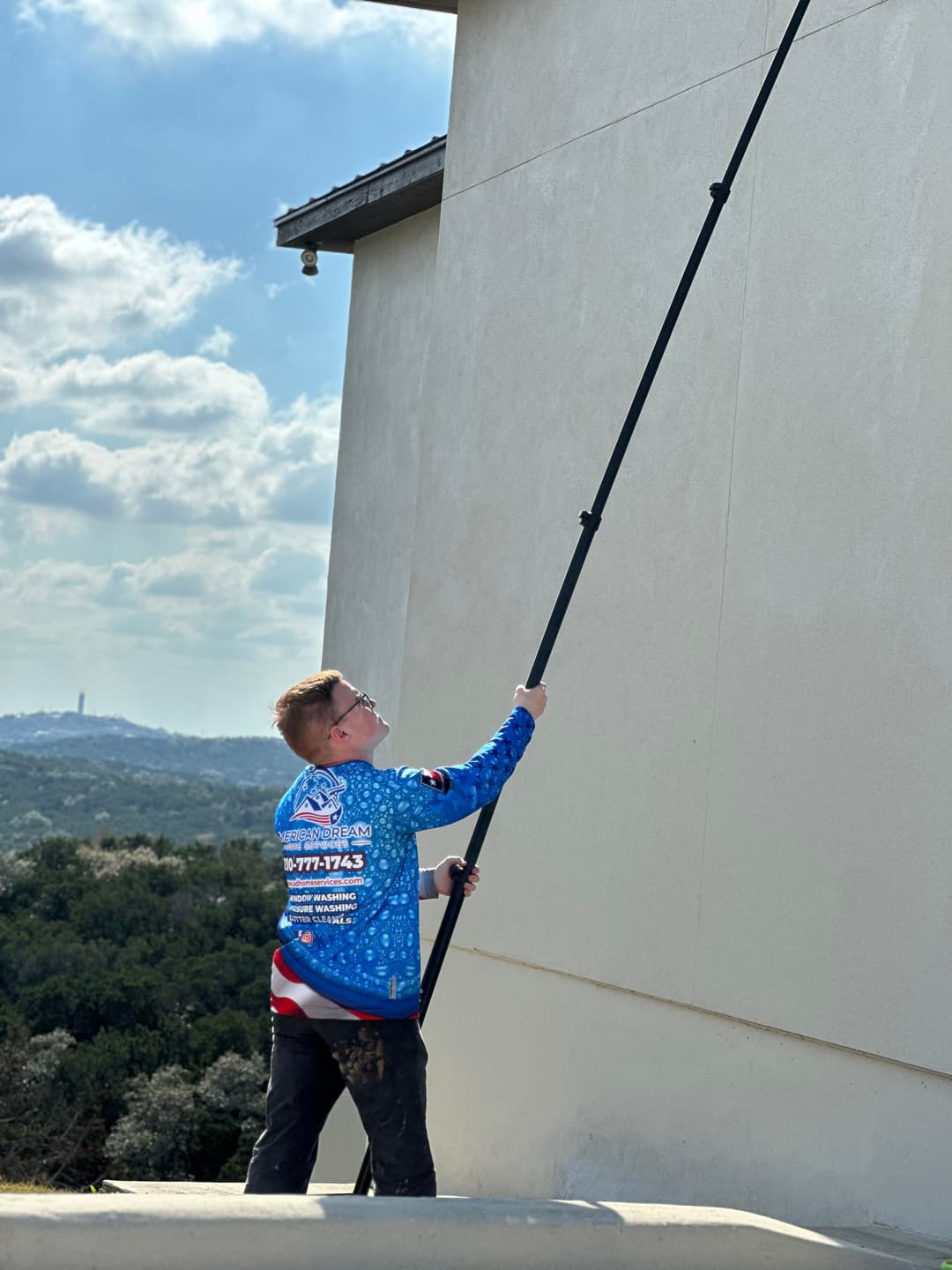 Child using a paint roller on a tall wall, wearing a colorful shirt and glasses.