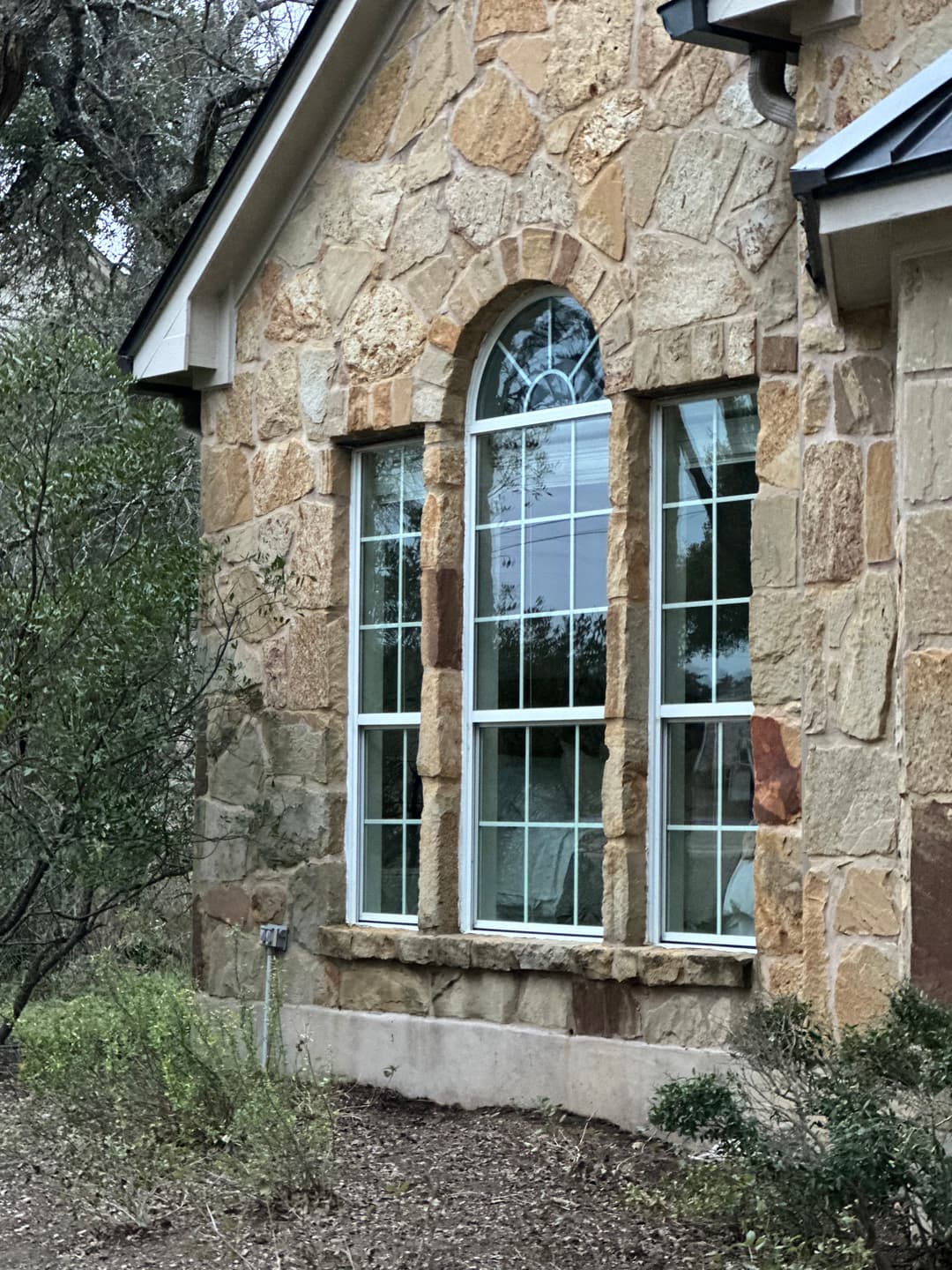 Stone house exterior featuring an arched window surrounded by greenery.