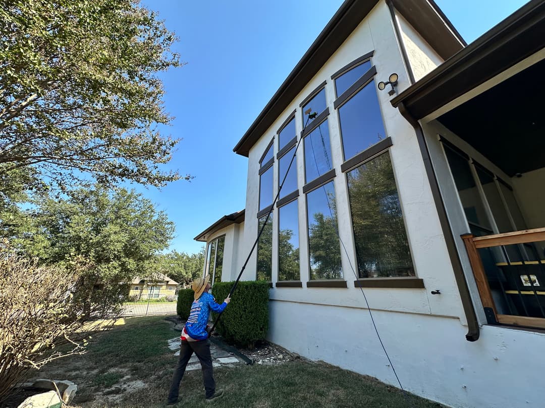 Person cleaning large windows on a modern house with a pole on a sunny day.