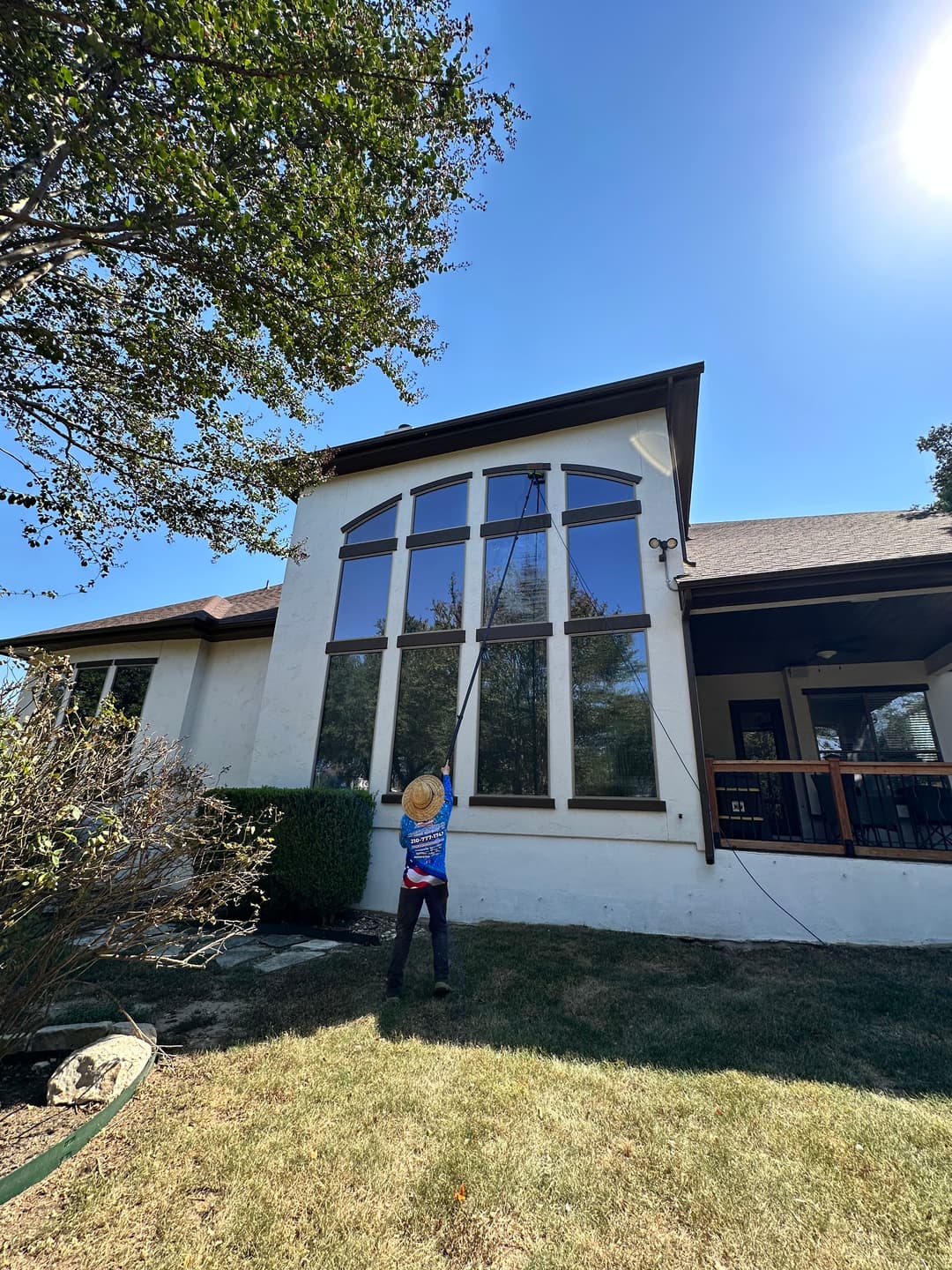 Child cleaning large windows on a house with a pole under clear blue sky.