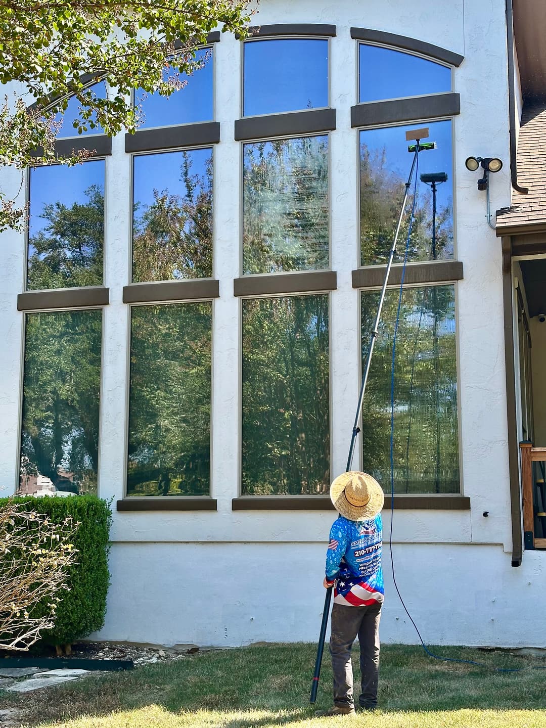 Professional window cleaner using a pole squeegee on large residential windows.