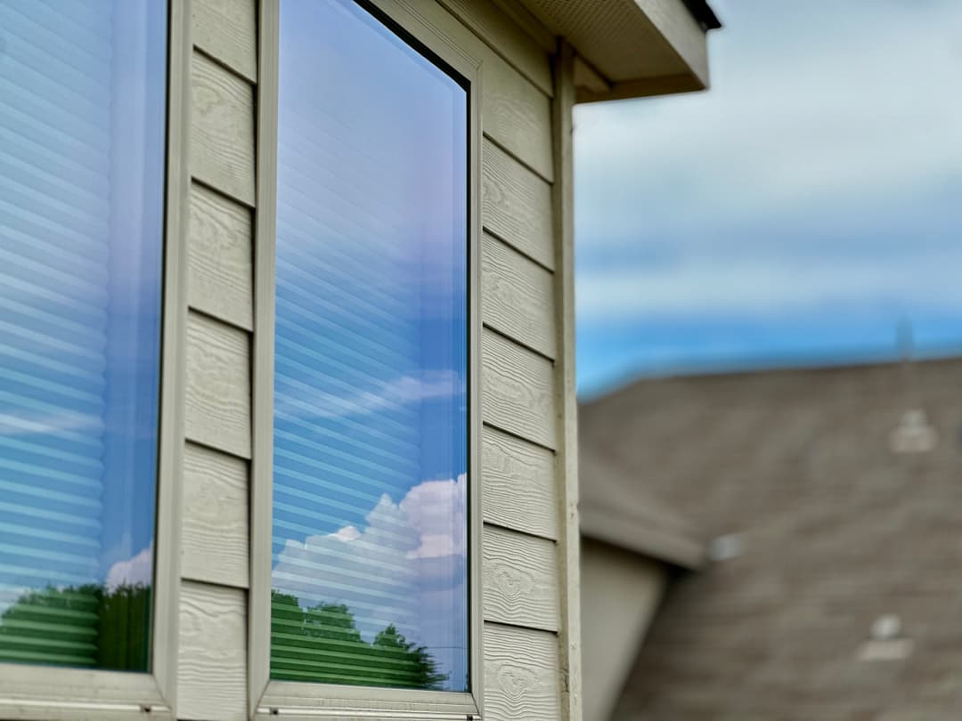 Close-up of a window reflecting clouds and greenery, showcasing modern home exterior design.