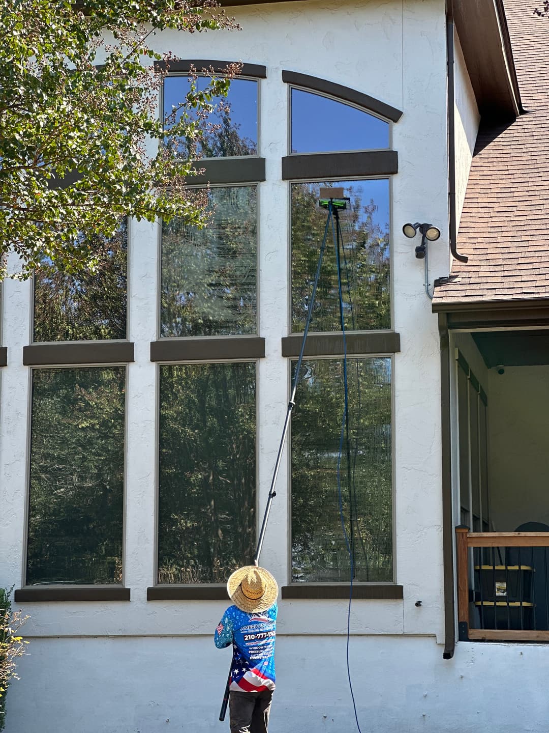 Window cleaner using a pole to wash large windows on a modern home exterior.