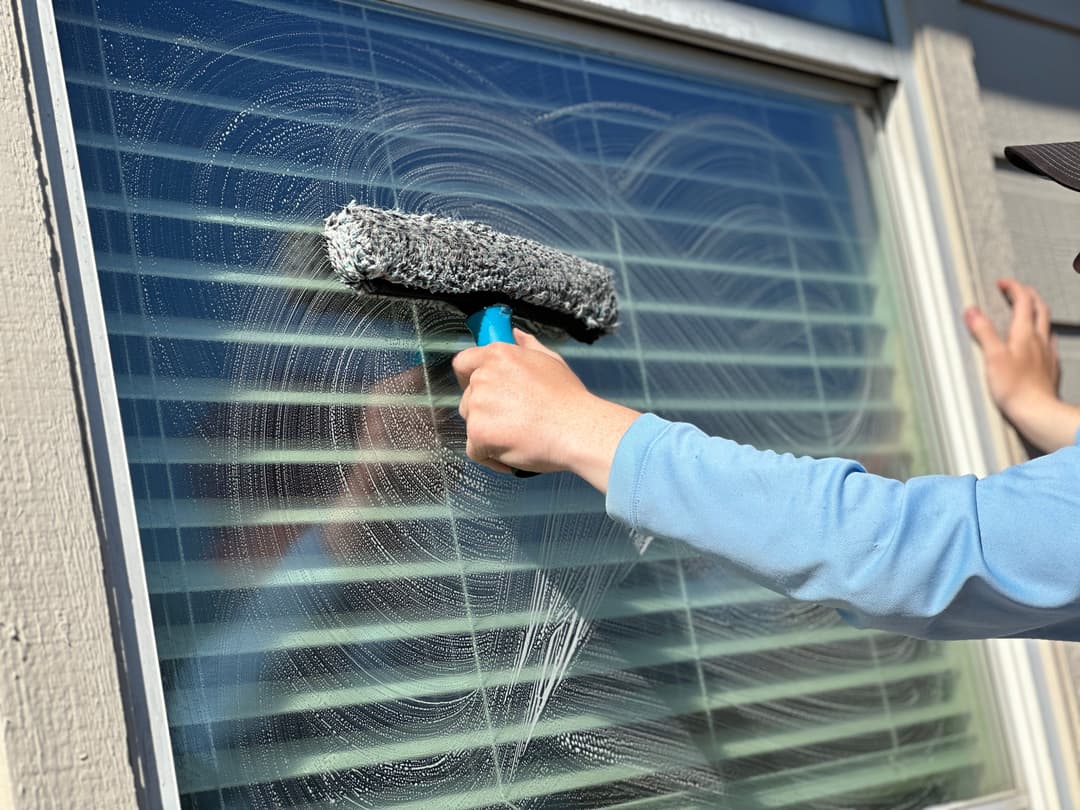 Person cleaning window blinds with a squeegee, showcasing effective home maintenance.