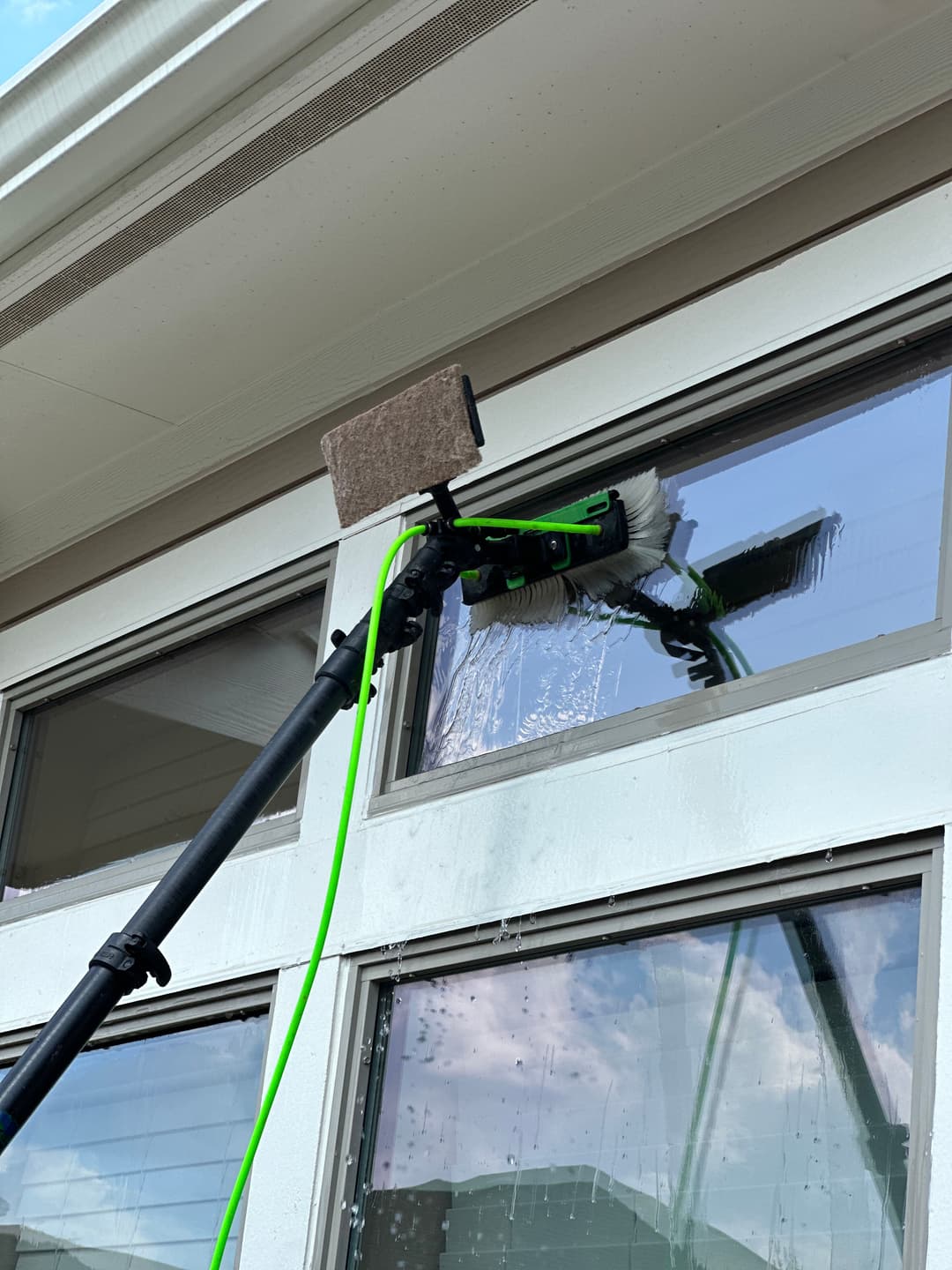 Window cleaning tool with a long handle and brush, reaching high glass panes outdoors.