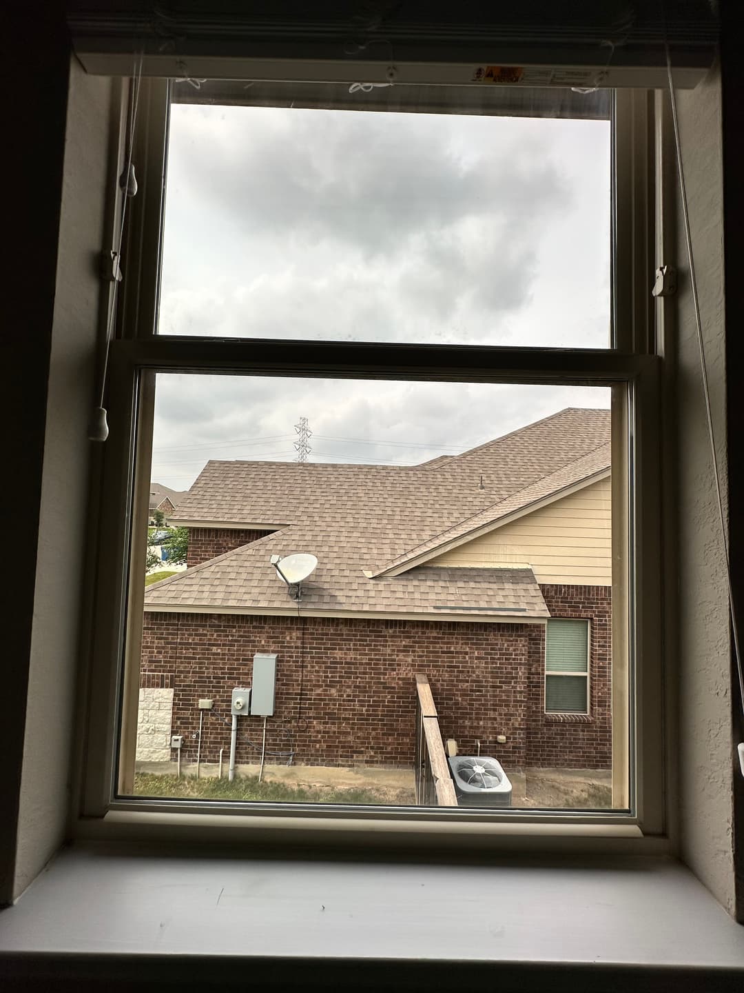 View through a window showing a backyard with houses and cloudy sky.