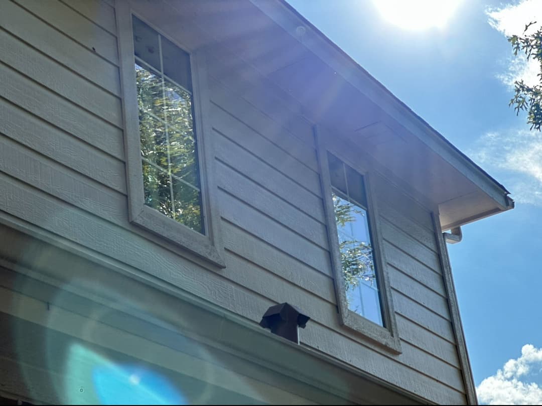Sunlit house exterior featuring prominent windows and a clear blue sky.
