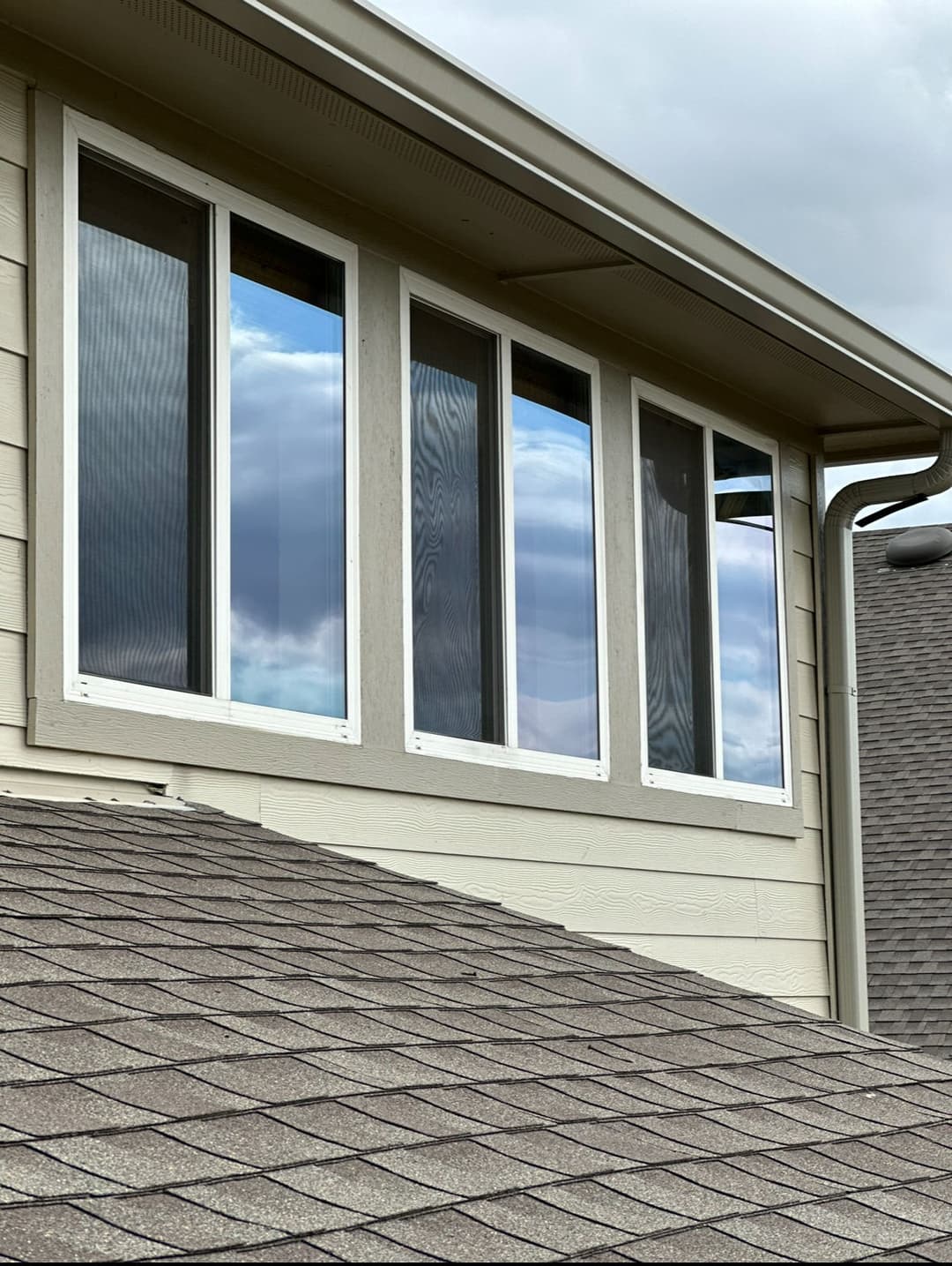 Modern multi-pane window on a house with a sloped roof and cloudy sky reflection.