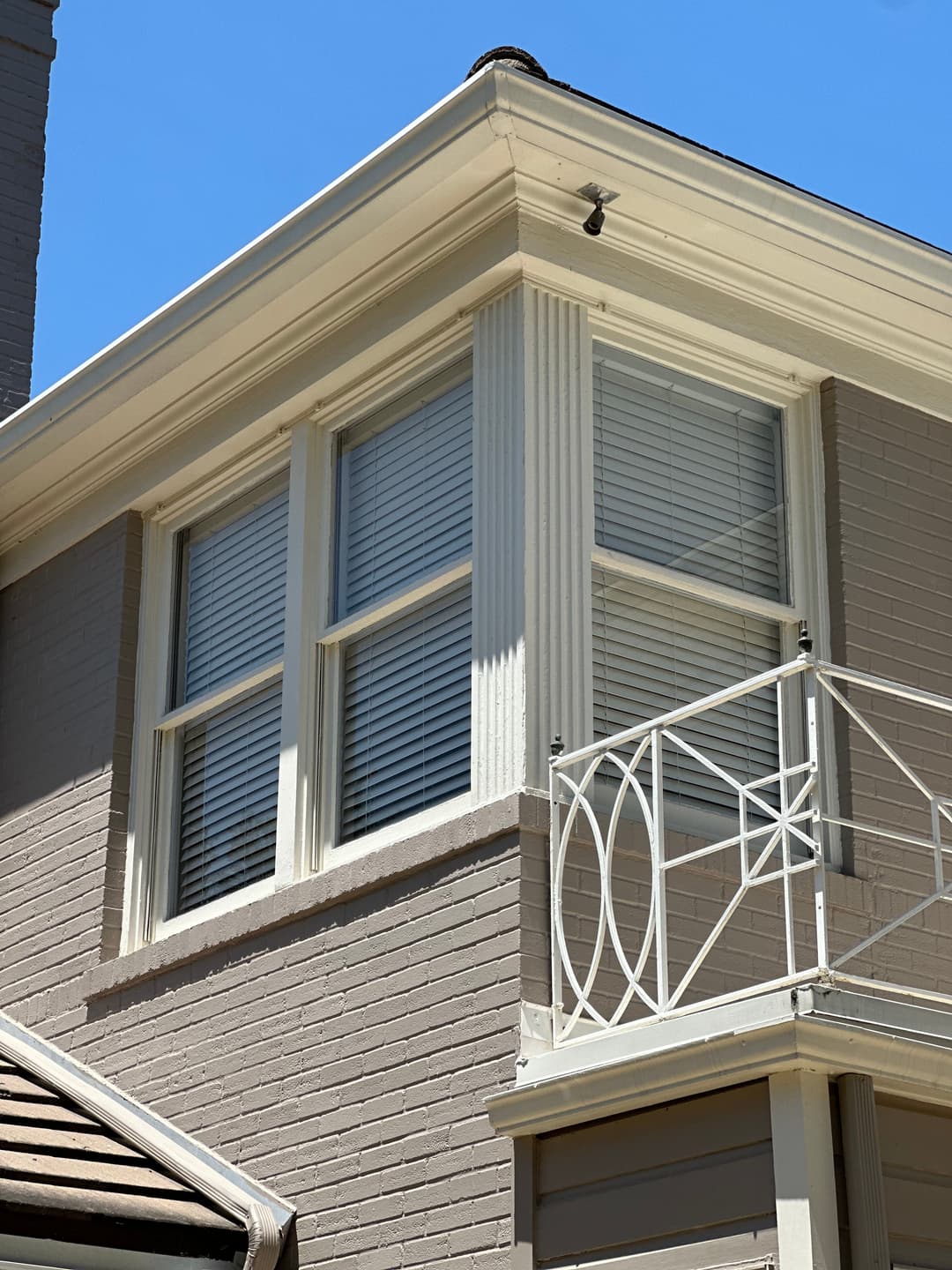 Modern house corner with decorative balcony and white window shutters against a clear blue sky.