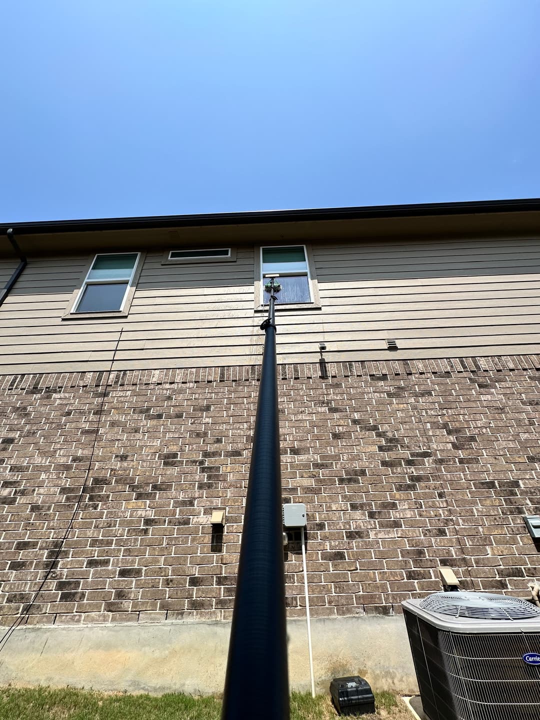 Pole extending towards a residential home's second story under clear blue sky.