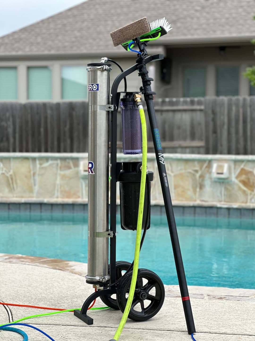 Pool cleaning equipment with a filter, brush, and hoses, positioned by a swimming pool.