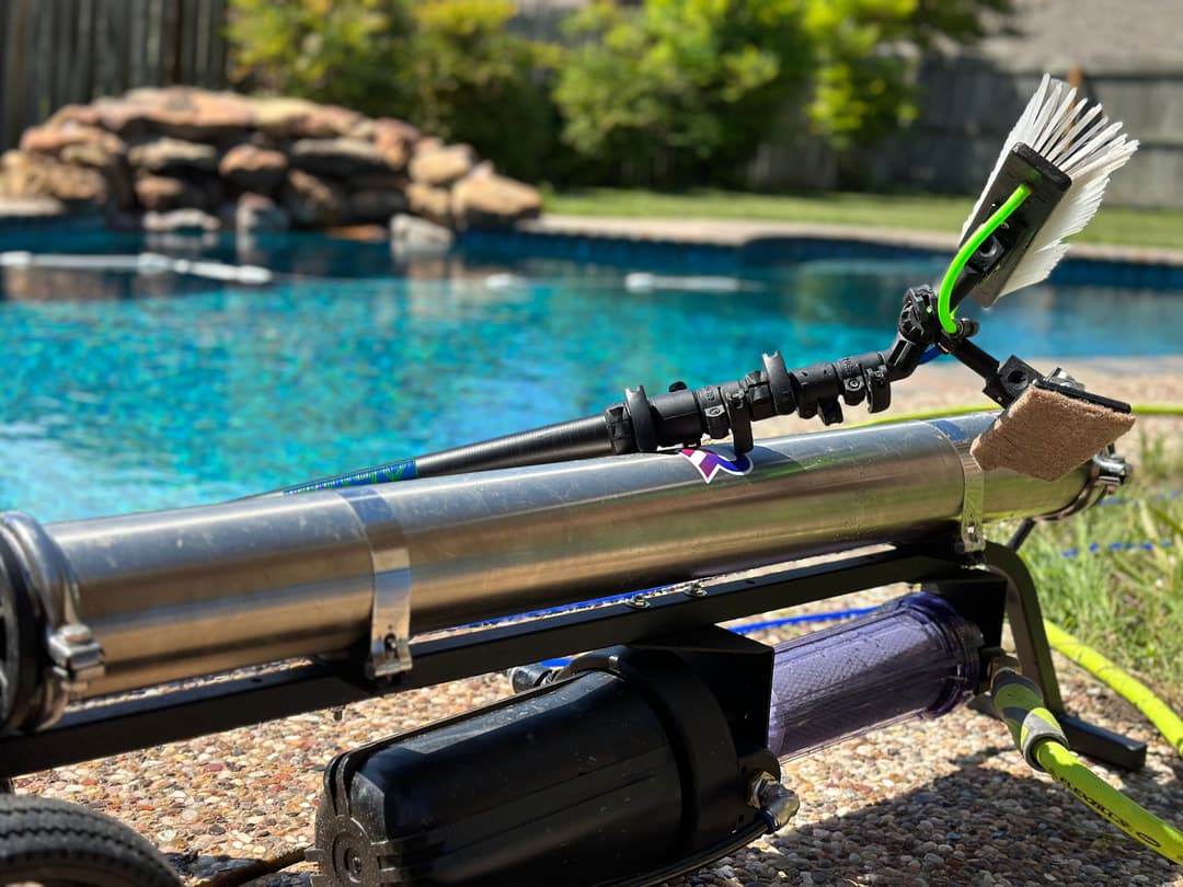 Pool cleaning equipment with a brush and hose near a clear blue swimming pool.
