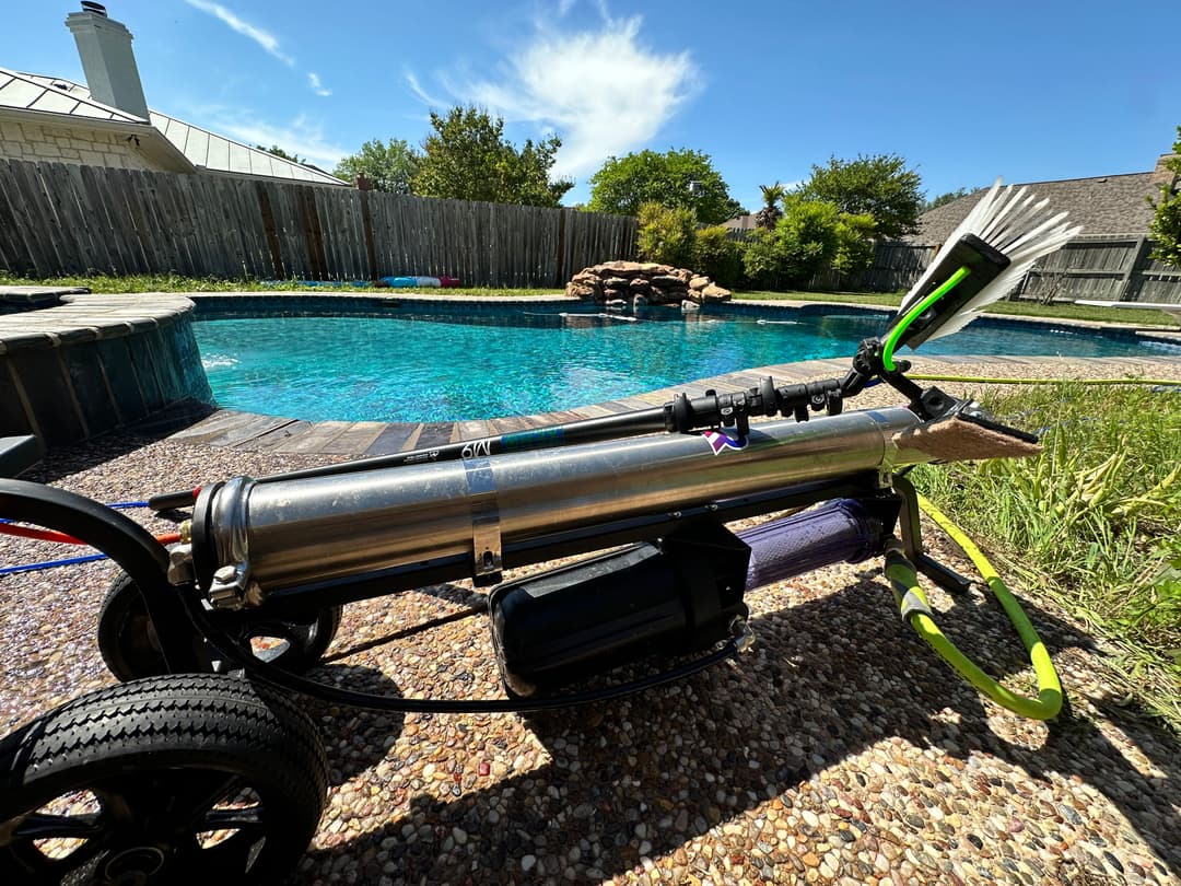 Pool cleaning robot beside a sparkling blue pool, featuring a sleek metallic design and efficient brush.