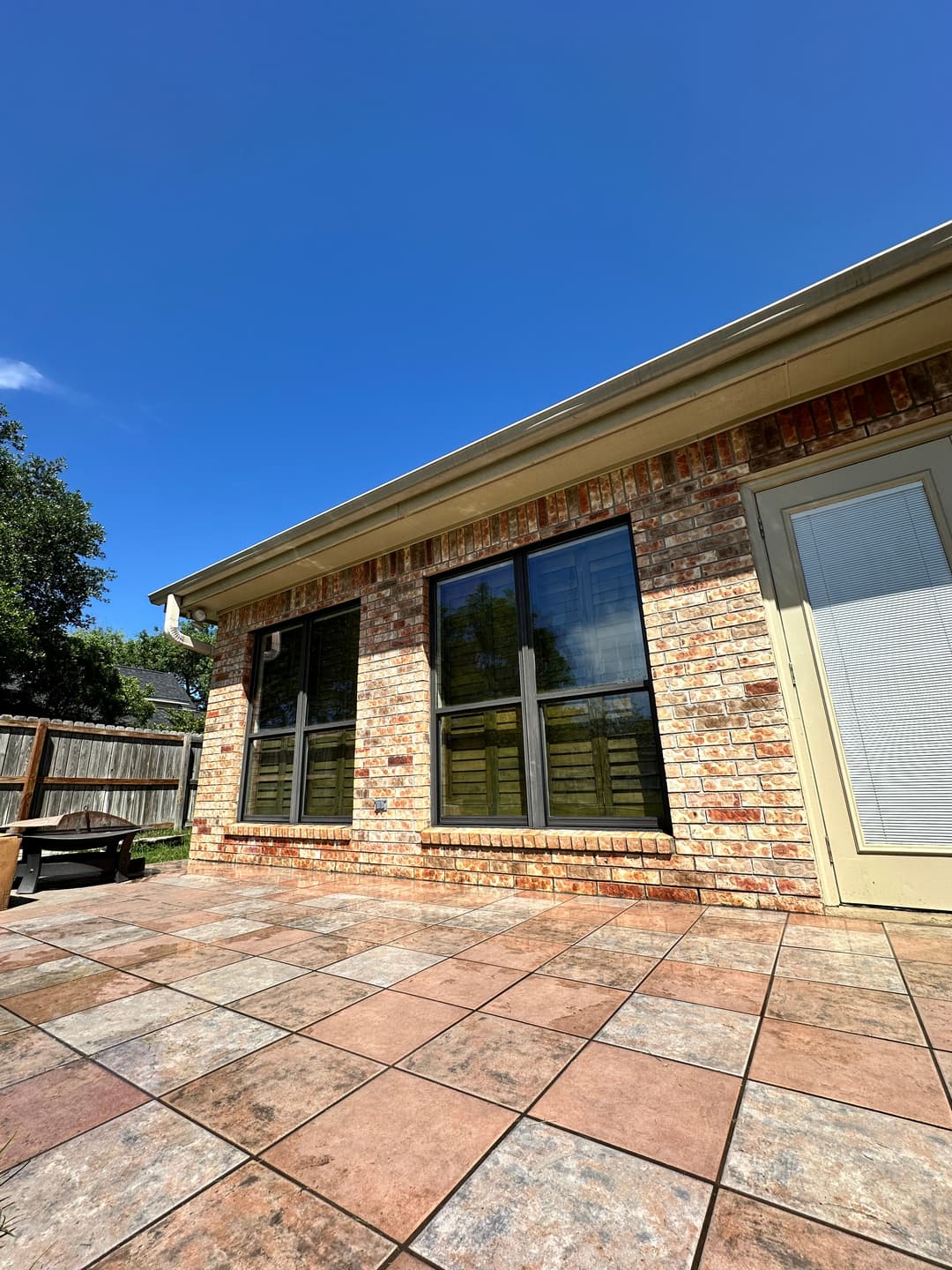 Brick house exterior with large windows and tiled patio under clear blue sky.