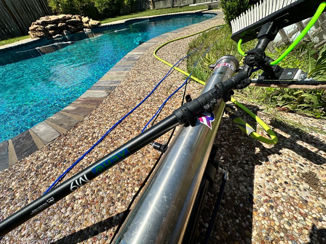 Pool cleaning equipment beside a shimmering blue pool with a stone border and lush greenery.