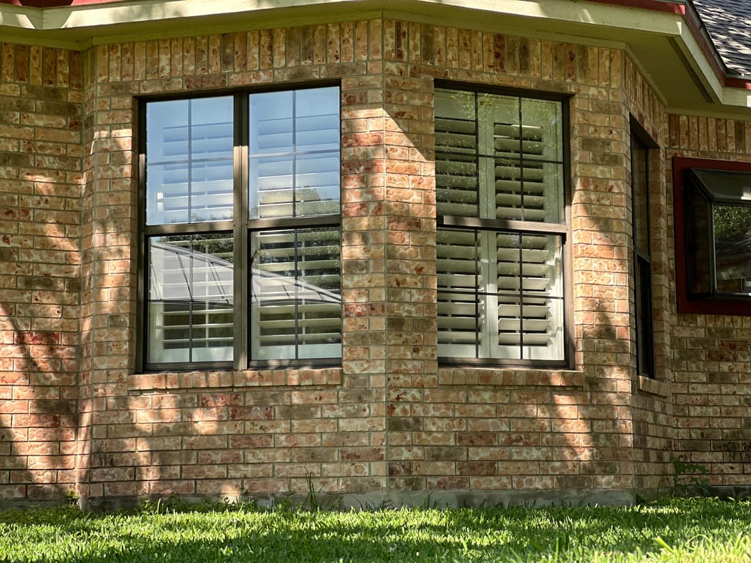 Brick home exterior featuring large, elegant windows with shutters and grassy lawn.