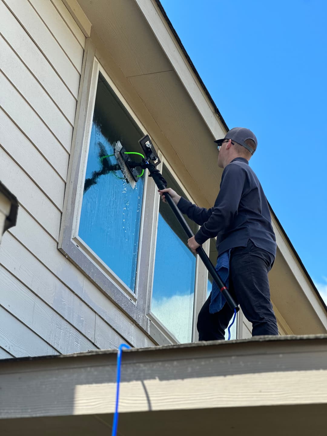 Person cleaning a window with a water-fed pole from an elevated platform on a sunny day.