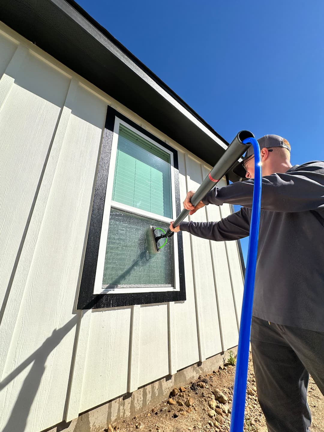 Man cleaning a window with a long reach squeegee on a modern house exterior.