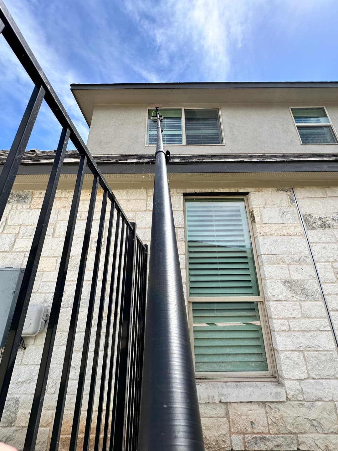 Pole reaching towards the window of a house, with blue sky and clouds in the background.