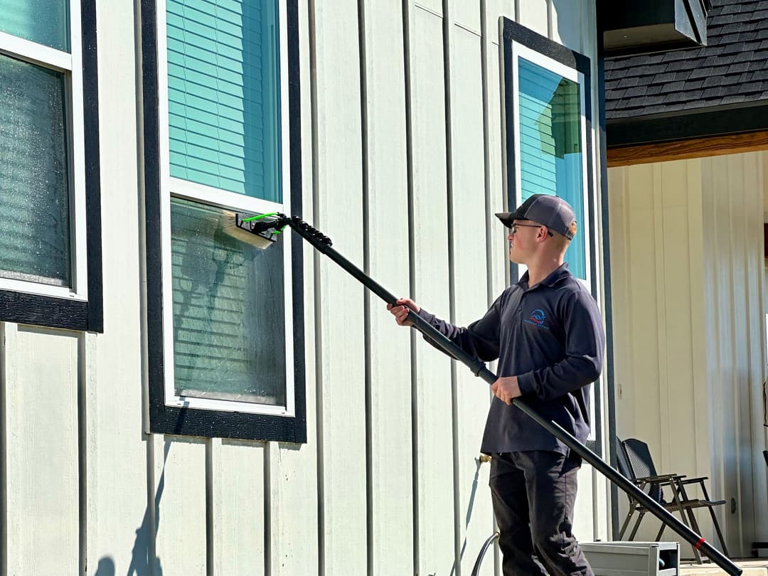 Worker using a pole to clean windows on a modern building.