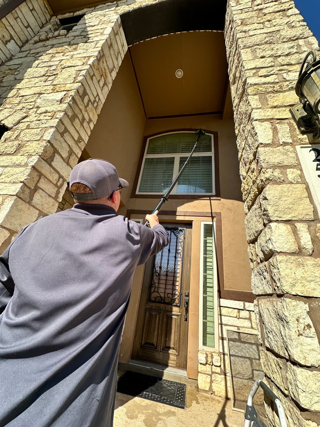 Man using a pole to clean the high entrance of a stone house. Bright sunny day.