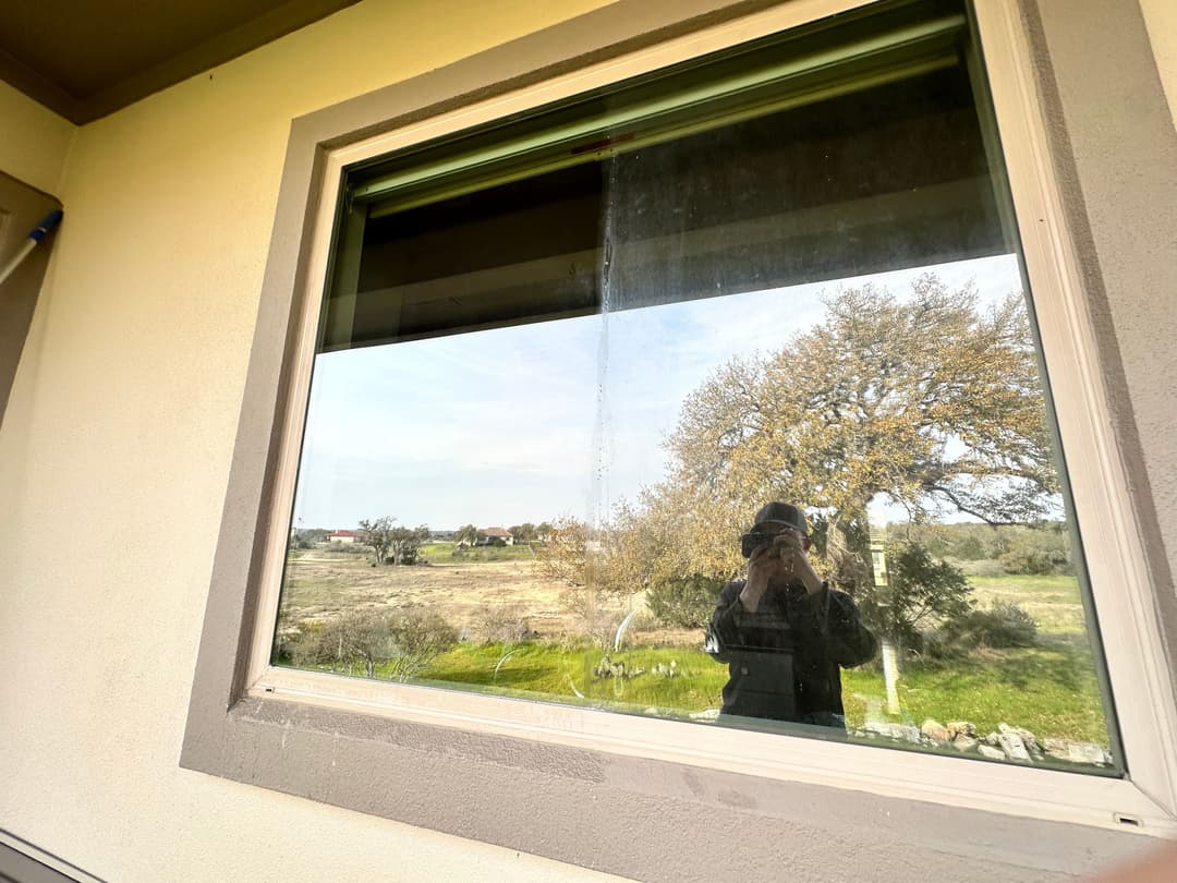 Reflection of a person in a window overlooking a scenic landscape with trees.