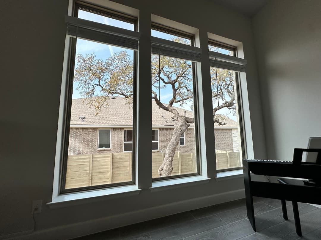Three large windows showcasing a tree outside a home, with a modern interior view.