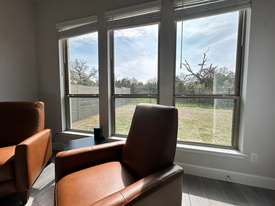 Cozy living room with leather chairs and large windows showcasing a sunny outdoor view.