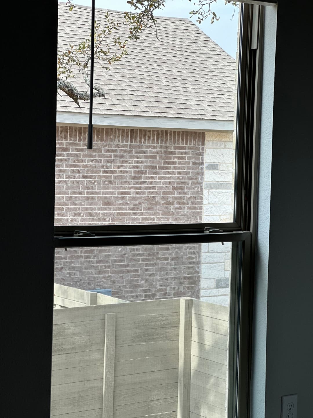 View from a window showing a brick wall and wooden fence in a residential area.