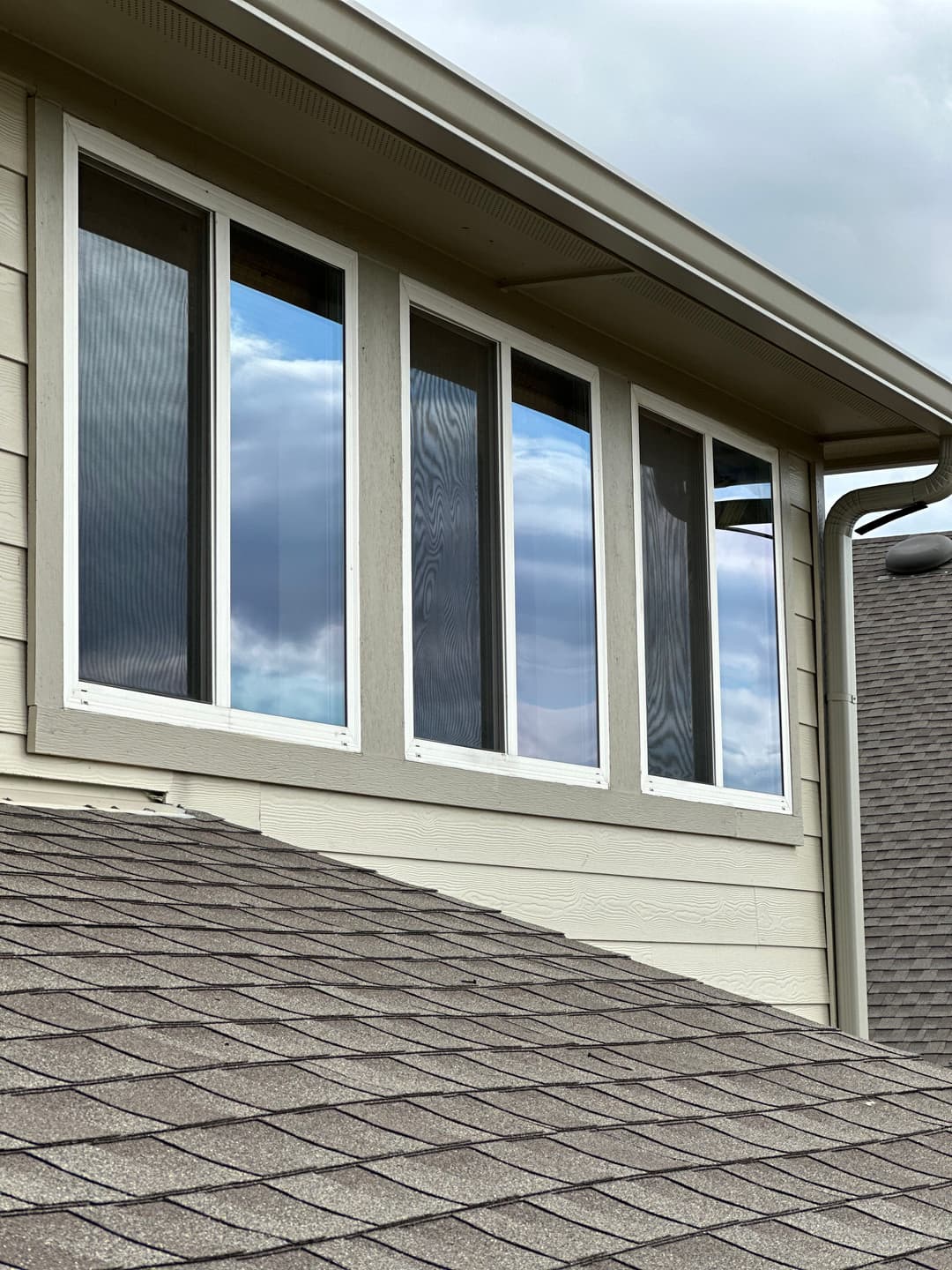 Modern house with four large windows reflecting cloudy sky and roof details.