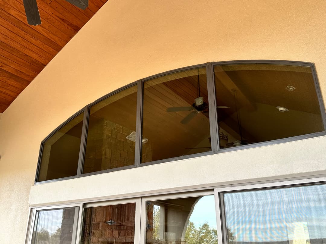 Large arched windows with wooden beams and ceiling fans in a modern home interior.