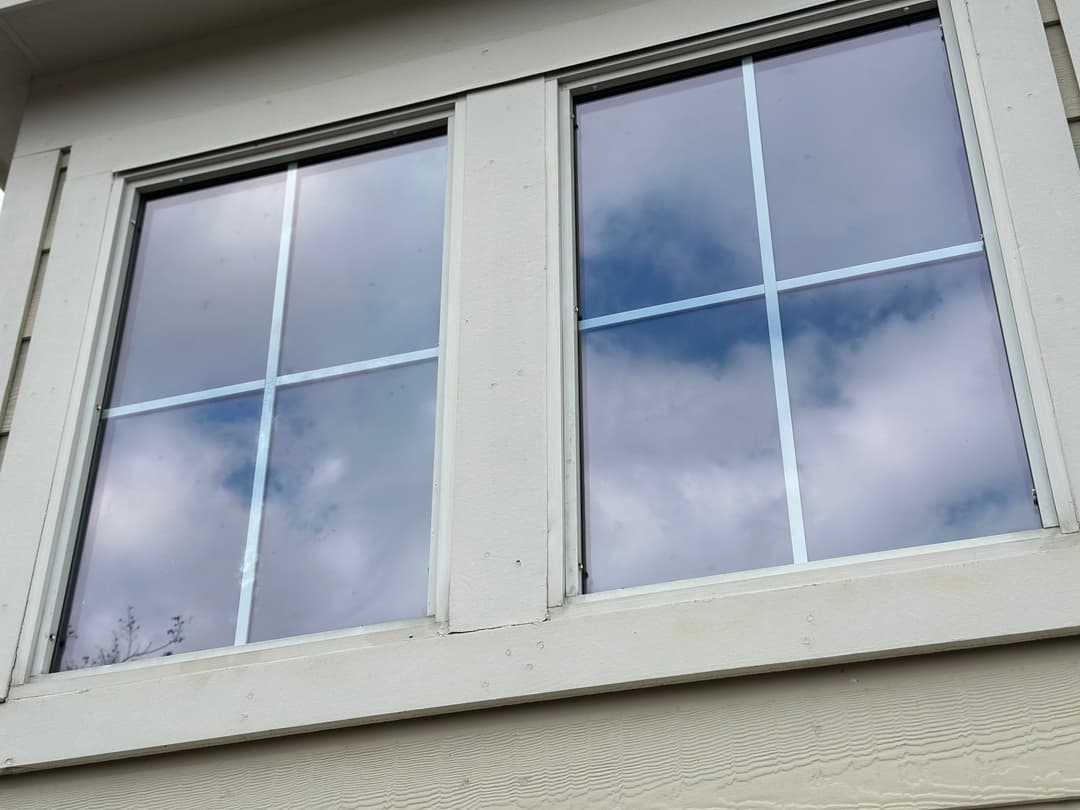 Two windows with a six-pane design reflecting cloudy skies.