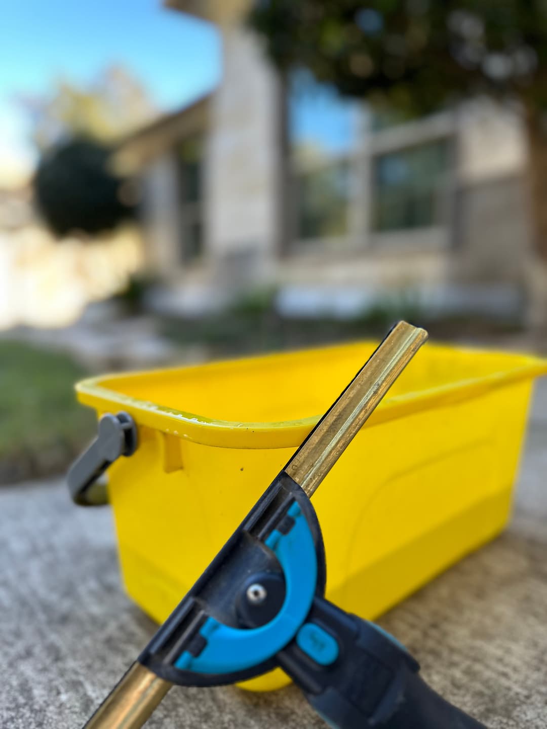 Yellow cleaning bucket with a squeegee in the foreground, set outside a building.