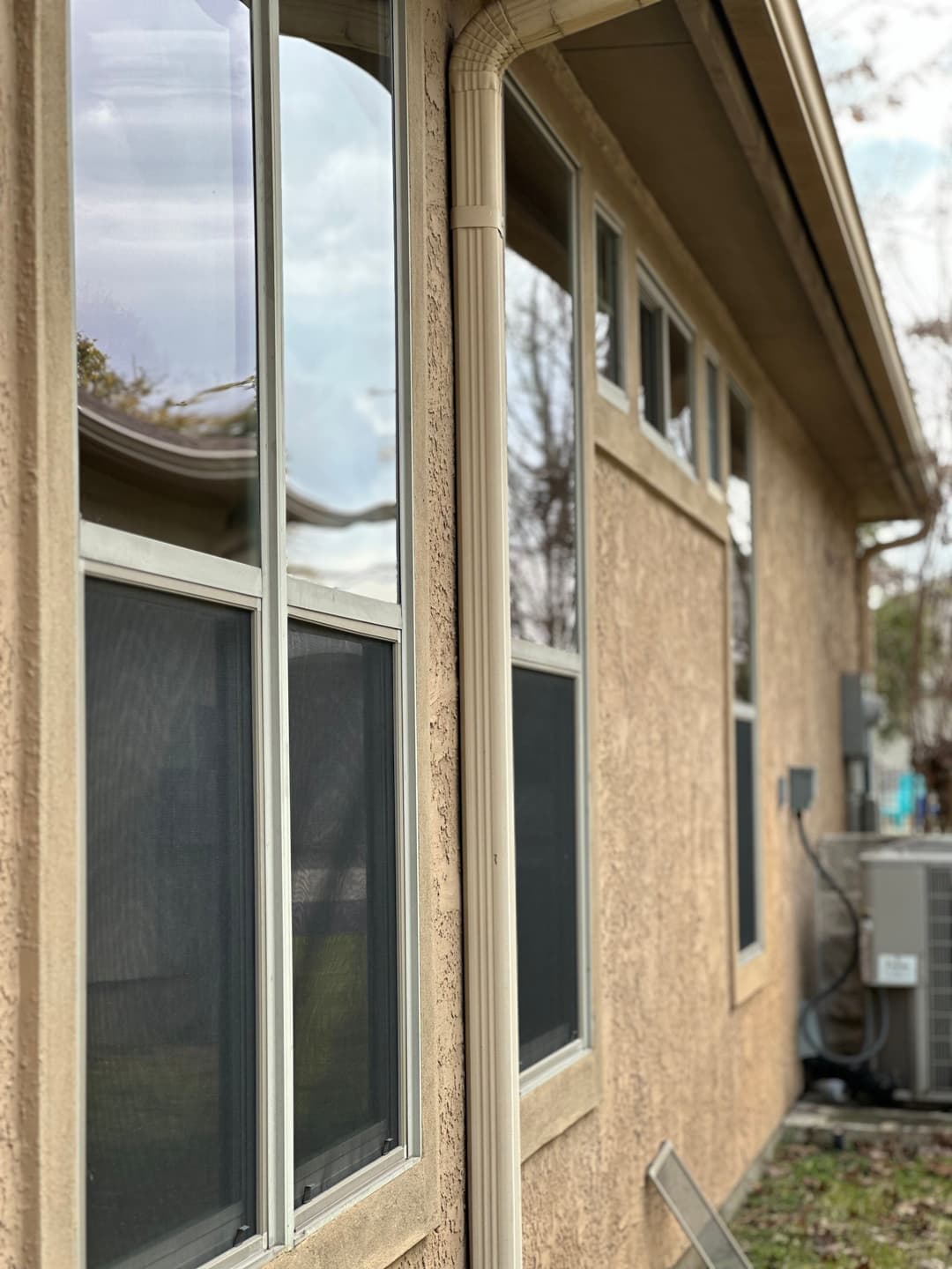 Side view of a house featuring windows, exterior walls, and a nearby air conditioning unit.