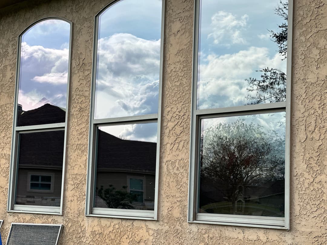 Three large windows reflecting clouds and trees on a textured beige wall.
