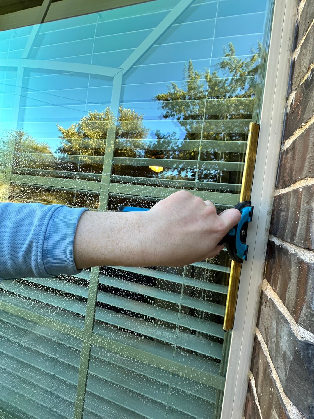 Hand using a window cleaning tool on a glass pane with visible water droplets and reflections.