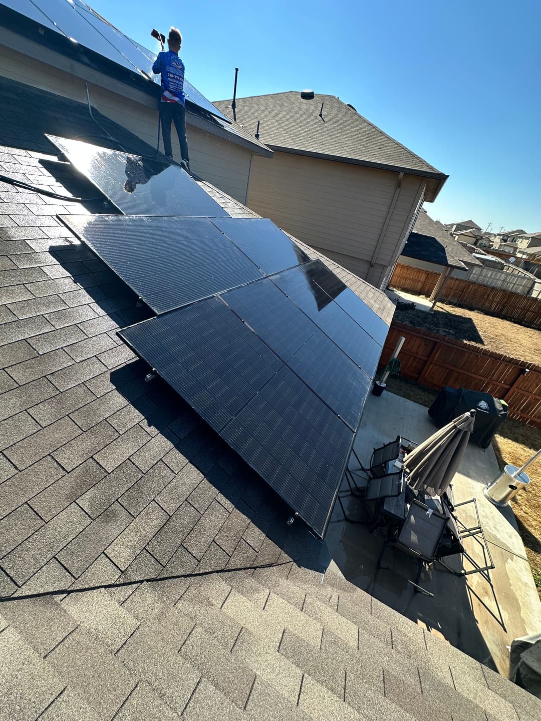 Worker installing solar panels on a residential roof with clear blue sky in the background.