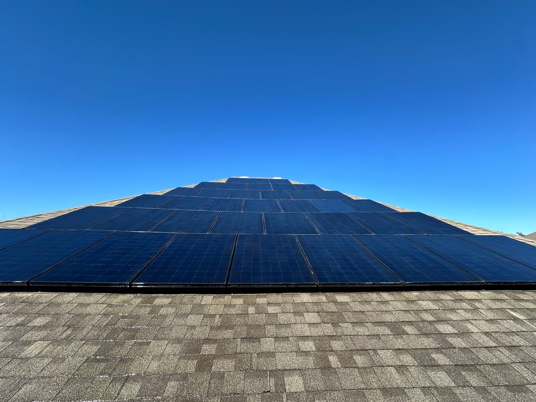 Solar panels on a sloped roof under a clear blue sky, promoting renewable energy use.