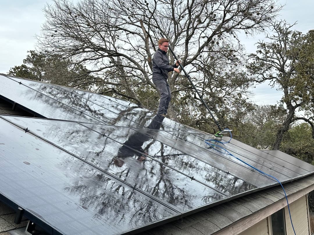 Worker cleaning solar panels on a rooftop with trees in the background.
