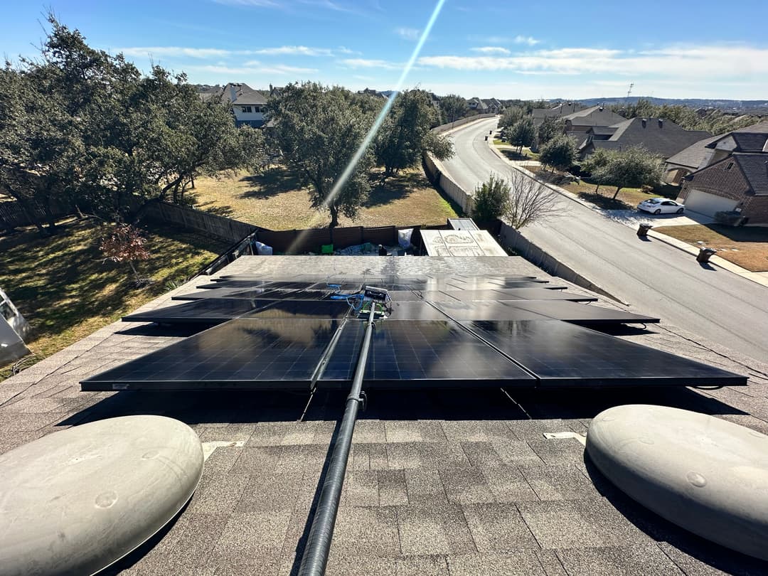 Aerial view of solar panels on a roof overlooking a residential street and landscape.