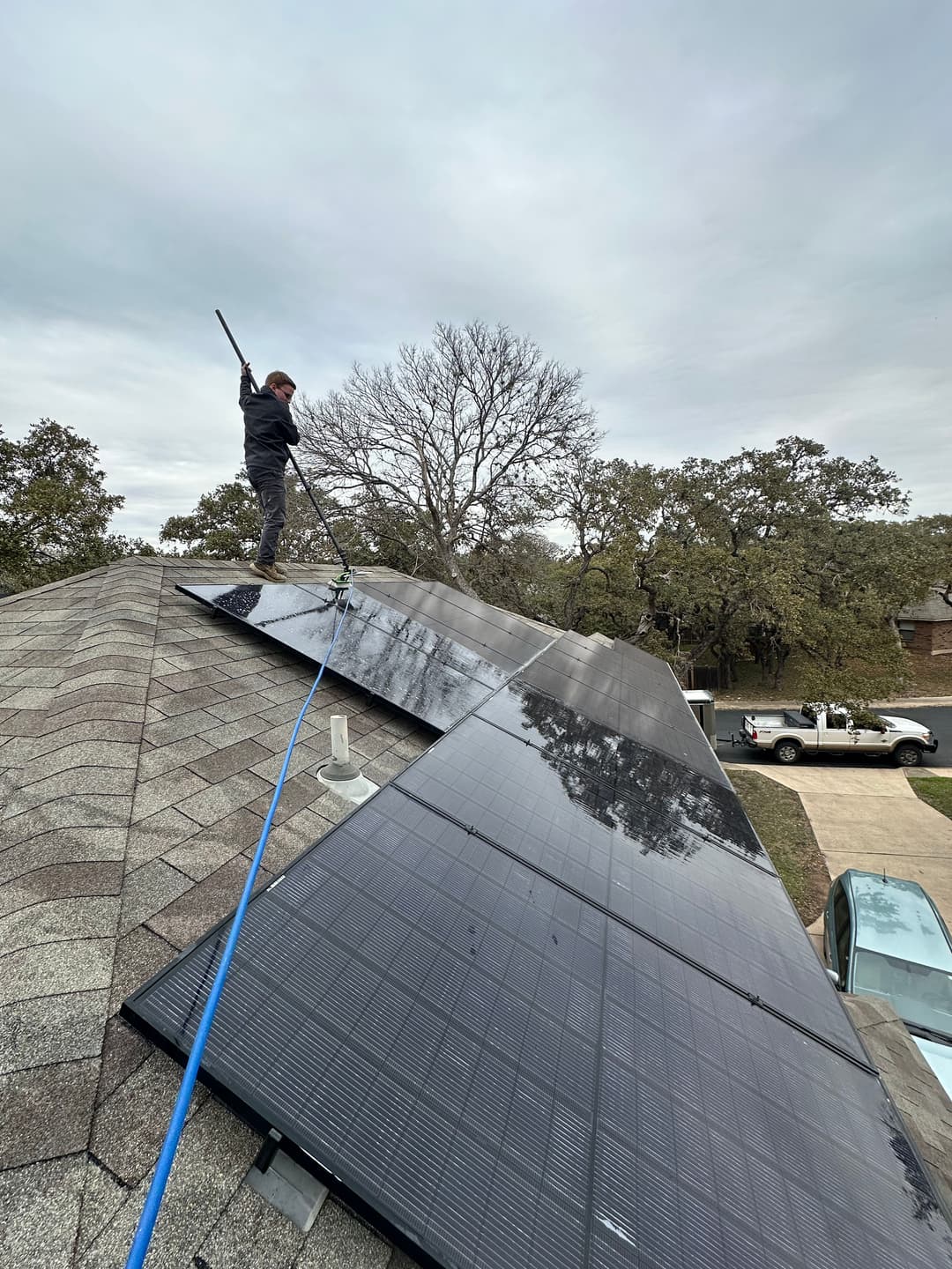 Technician cleaning solar panels on a roof, with trees and a pickup truck in the background.