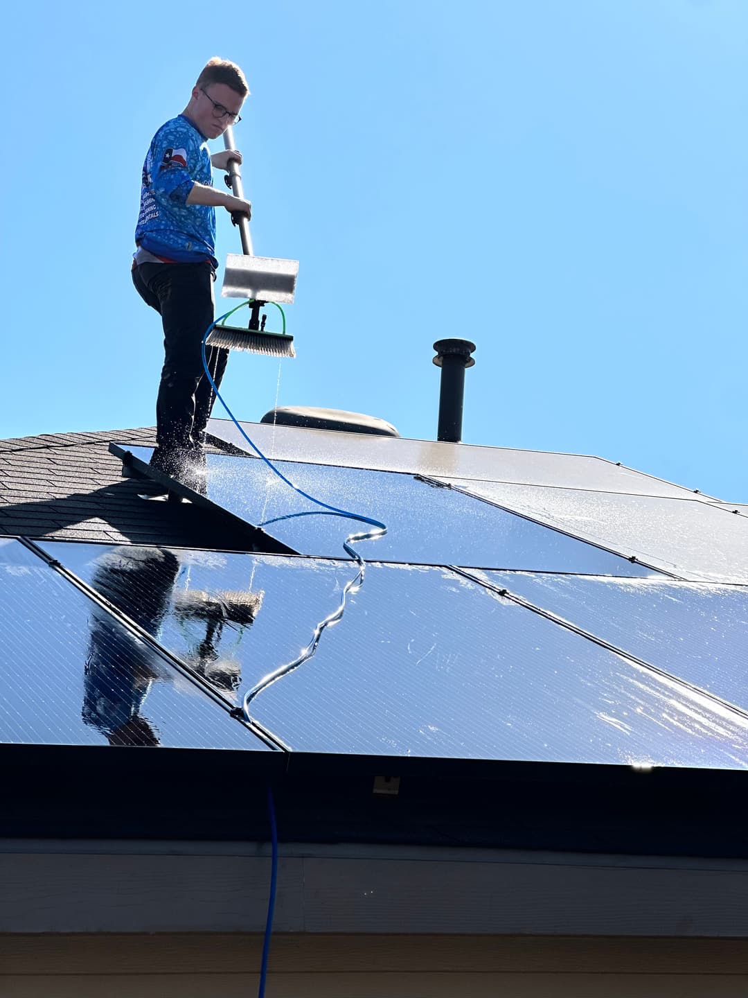 Person cleaning solar panels on a bright sunny day using a water-fed pole.
